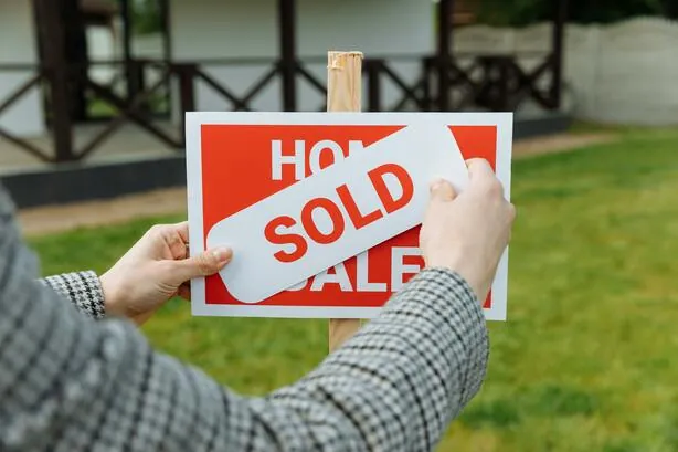 A realtor placing a SOLD sticker on a for-sale sign